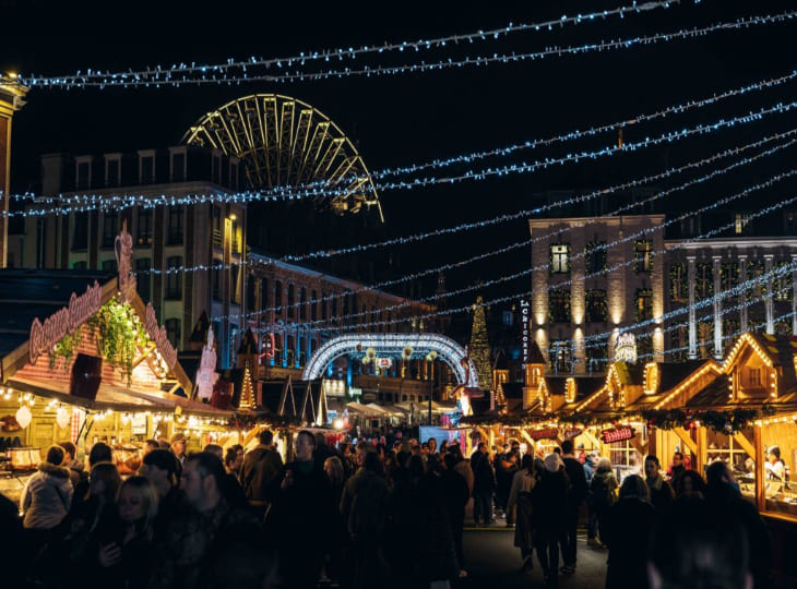 Chalets illuminés et Grande Roue du Marché de Noël de Lille de nuit, ambiance de fête en centre-ville.
