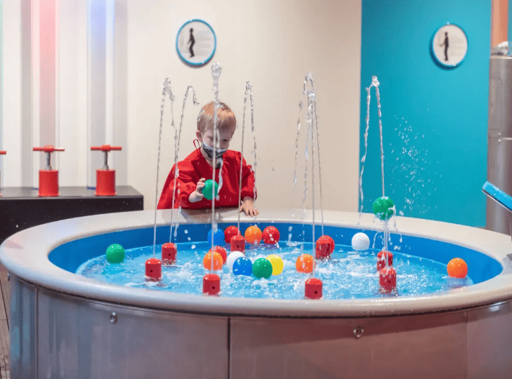 Enfant jouant avec des jets d'eau et des balles à Smallicieux, la cité des enfants de Lillenium à Lille.