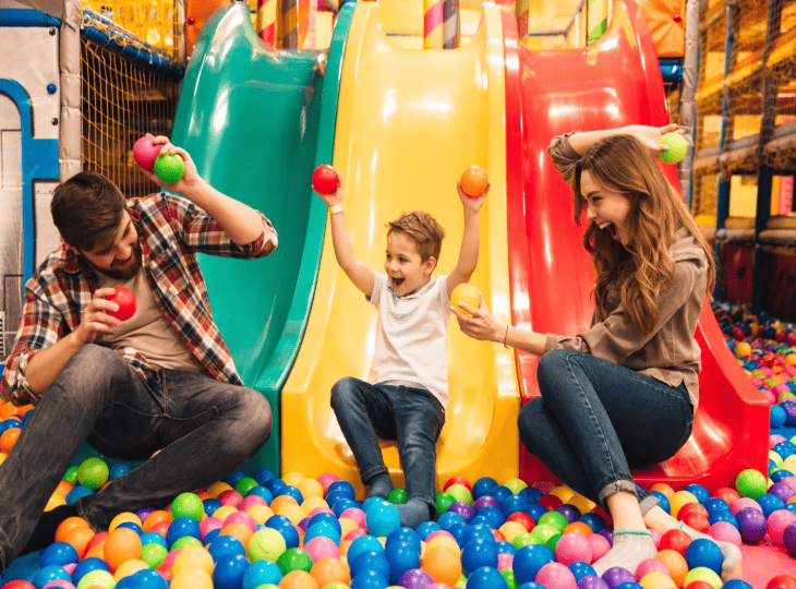 Famille jouant dans une piscine à balles avec toboggans colorés au Gulli Parc Lille, parc de jeux couvert pour enfants.